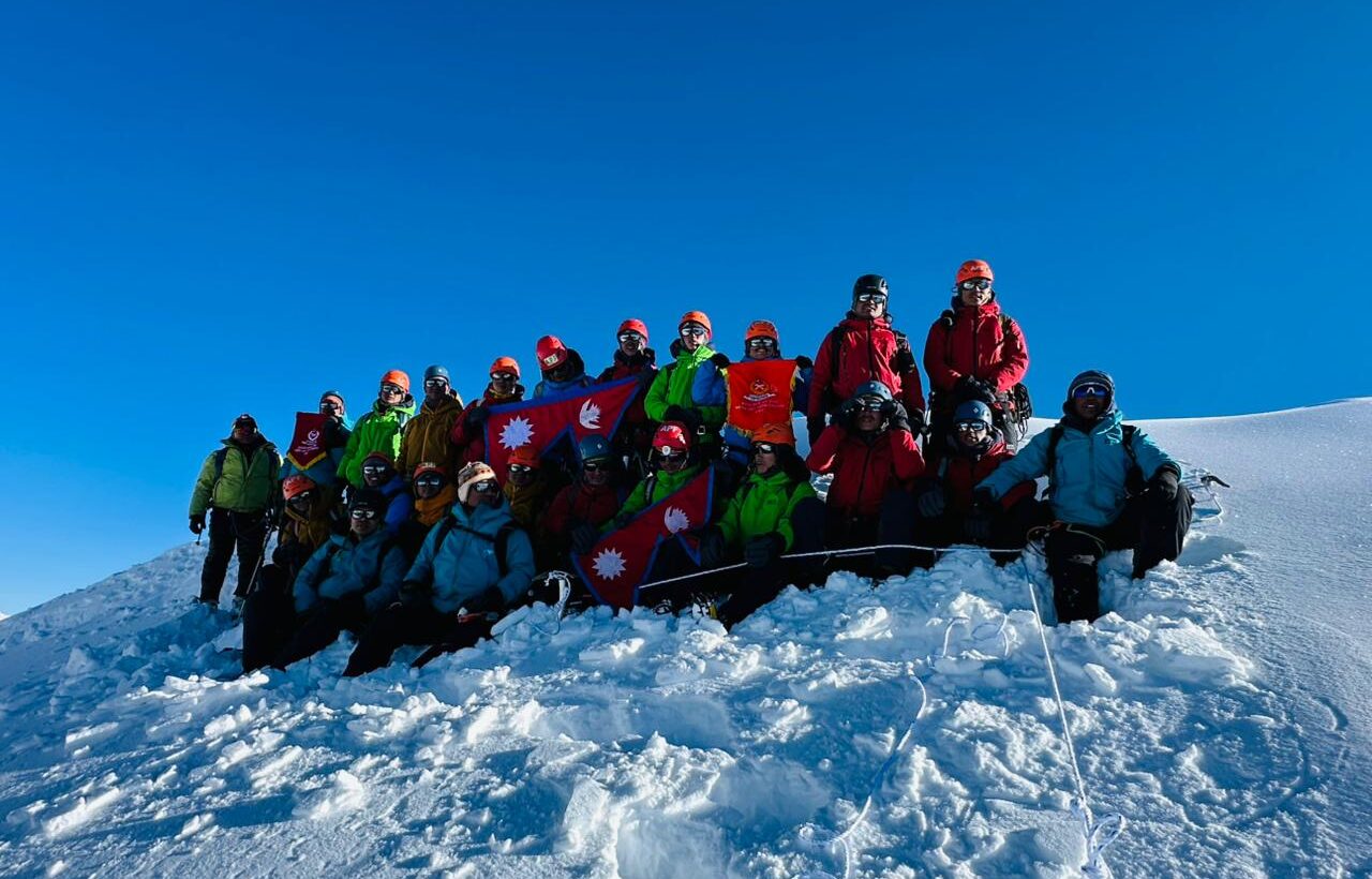 Climbers with Nepal flags on the snowy summit of Chulu East Peak under a clear blue sky.