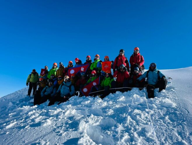 Climbers with Nepal flags on the snowy summit of Chulu East Peak under a clear blue sky.
