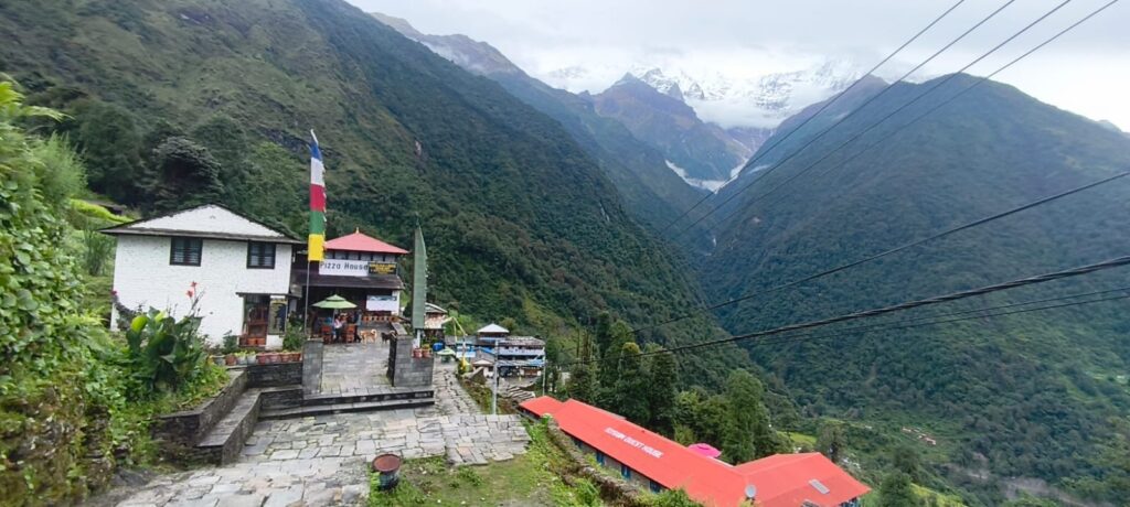 Scenic view of Chhomrong Village with mountain lodges and green hills.